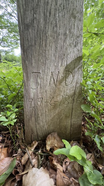 The inscription J N D and 29-6-1856 carved into a weathered wooden cross